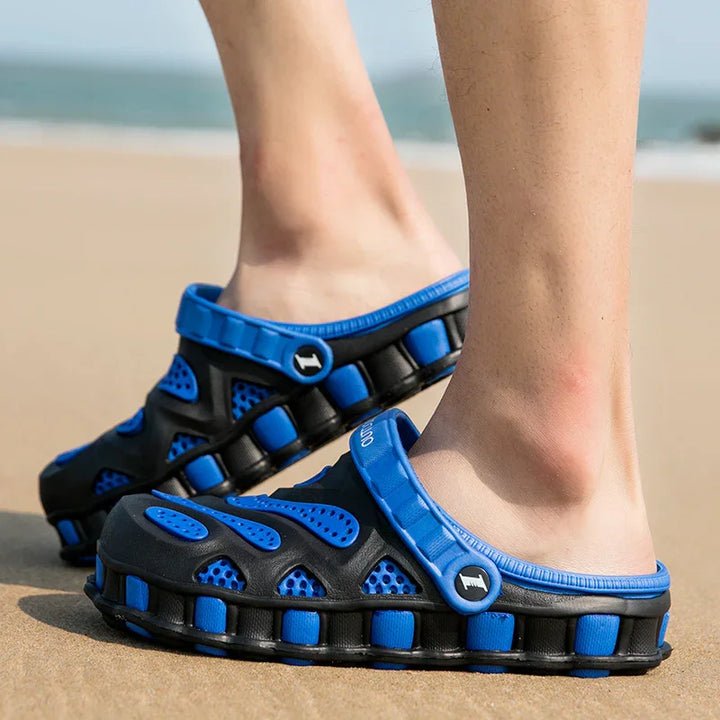 Close-up of blue and black breathable slip-on beach sandals worn outdoors on sand