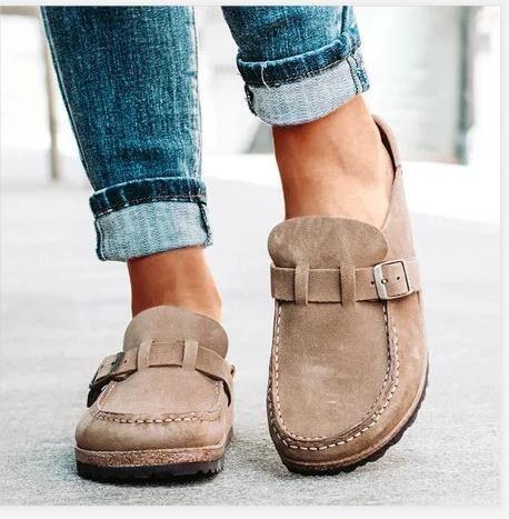 close-up of feet wearing beige suede casual slip-on shoes with buckle detail and rolled-up blue jeans outdoors