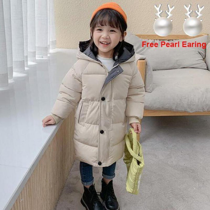 Smiling child wearing beige puffer coat, orange hat, black boots, holding yellow bag indoors
