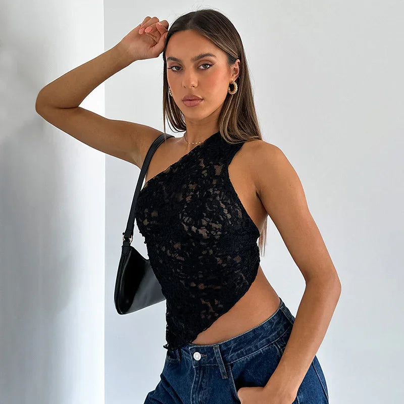 Woman wearing black lace one-shoulder top and high-waisted blue jeans posing with black shoulder bag