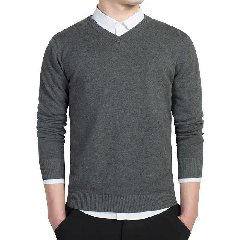 Man wearing fitted charcoal gray V-neck sweater over white collared shirt with hands in pockets