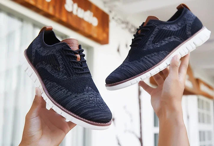 Hands holding black knit casual shoes with white soles and brown accents indoors