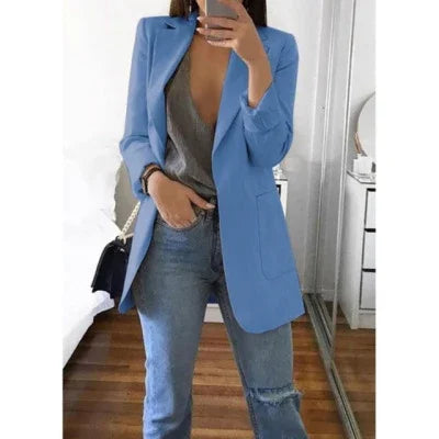 Woman wearing a light blue blazer over a gray top and ripped blue jeans in a modern bedroom