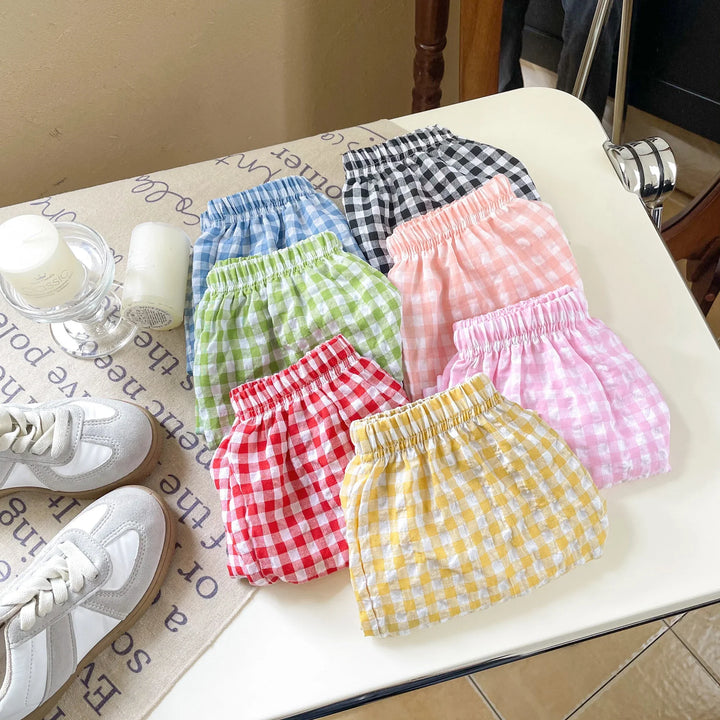 Colorful gingham check shorts folded on white table with candles and white sneakers nearby