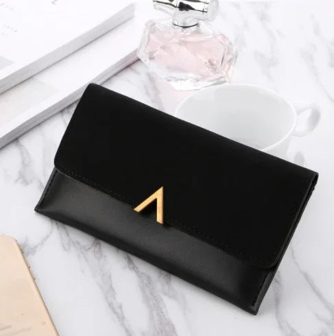 Elegant black leather wallet with gold clasp on marble table with perfume and white cup