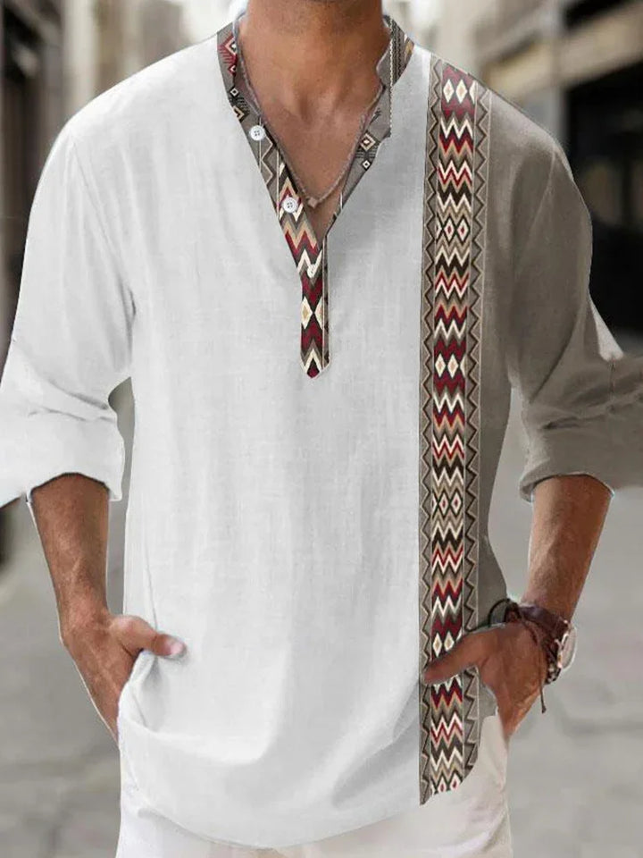 Man wearing white long sleeve shirt with tribal pattern on collar and vertical stripe, hands in pockets