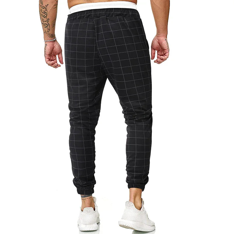 Back view of man wearing black checkered jogger pants with white sneakers and tattoos