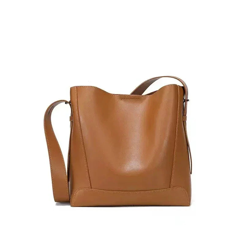 Minimalist tan leather bucket bag with adjustable shoulder strap on white background
