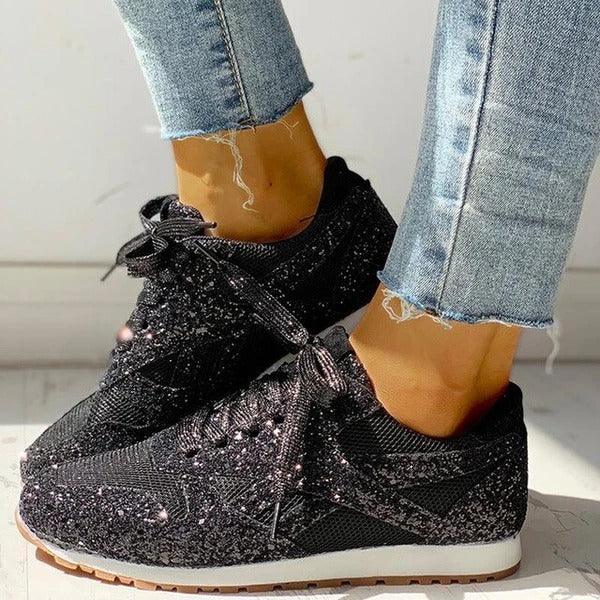 Black speckled knit sneakers with white soles worn with cuffed blue jeans on hardwood floor