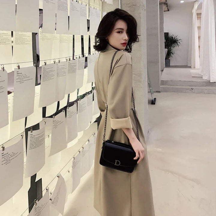 Woman in beige trench coat with black leather shoulder bag standing in art gallery with hanging white papers