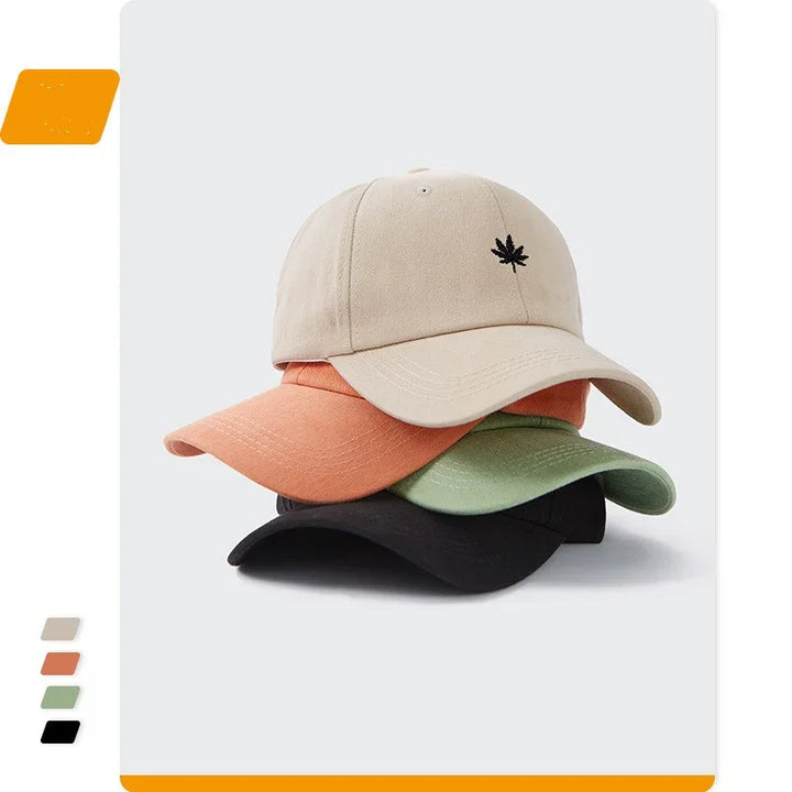 Stack of four baseball caps in beige with leaf logo, orange, green, and black on white background
