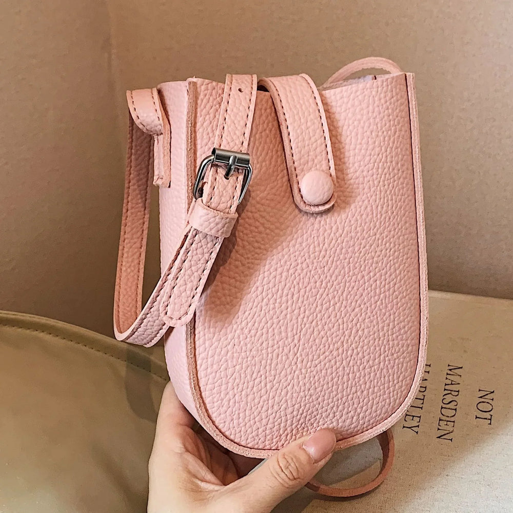 Hand holding a small textured pink leather crossbody bag with silver buckle strap