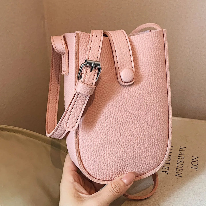 Hand holding a small textured pink leather crossbody bag with silver buckle strap