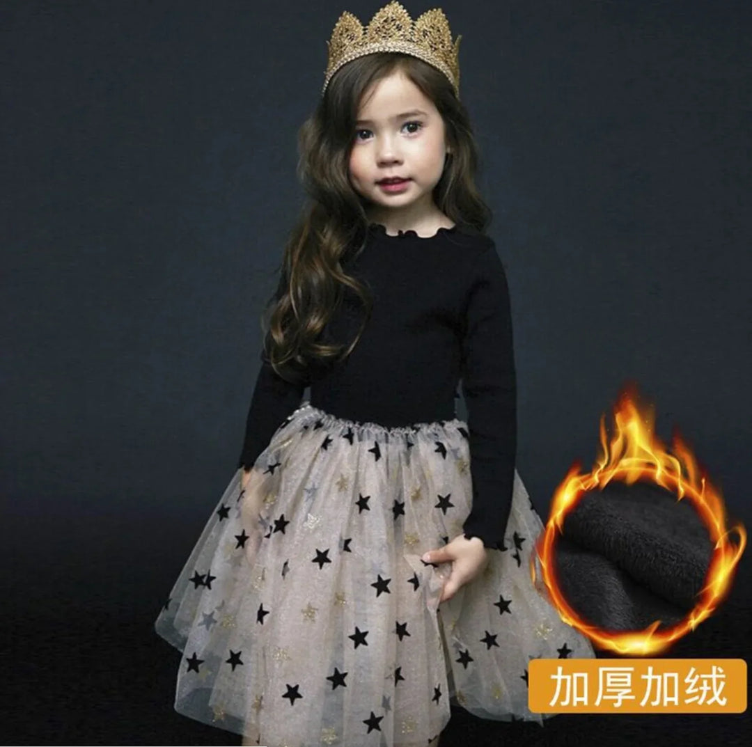 Young girl wearing a black long-sleeve top and star-patterned tulle skirt with a gold crown