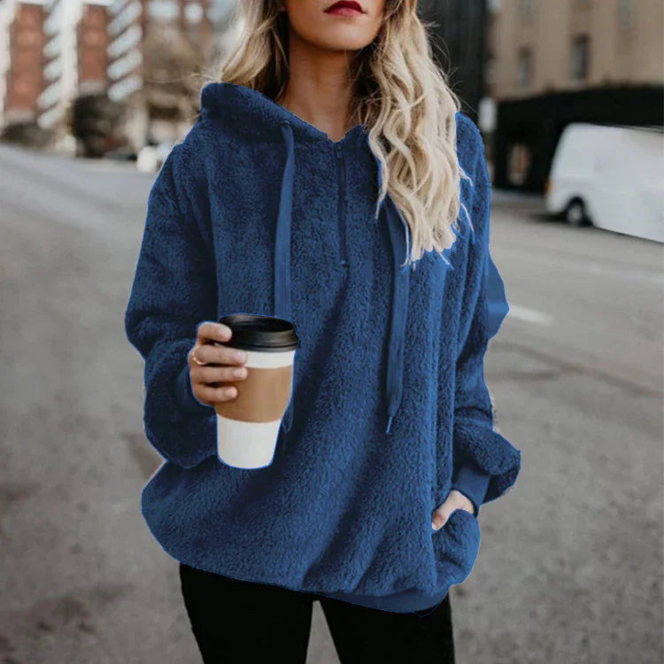 Woman wearing blue sherpa fleece hoodie holding a takeaway coffee cup on city street