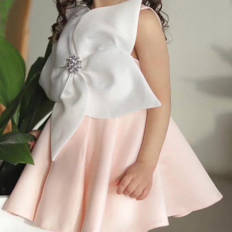 Close-up of a child wearing a pink dress with a large white flower decoration featuring a jeweled center