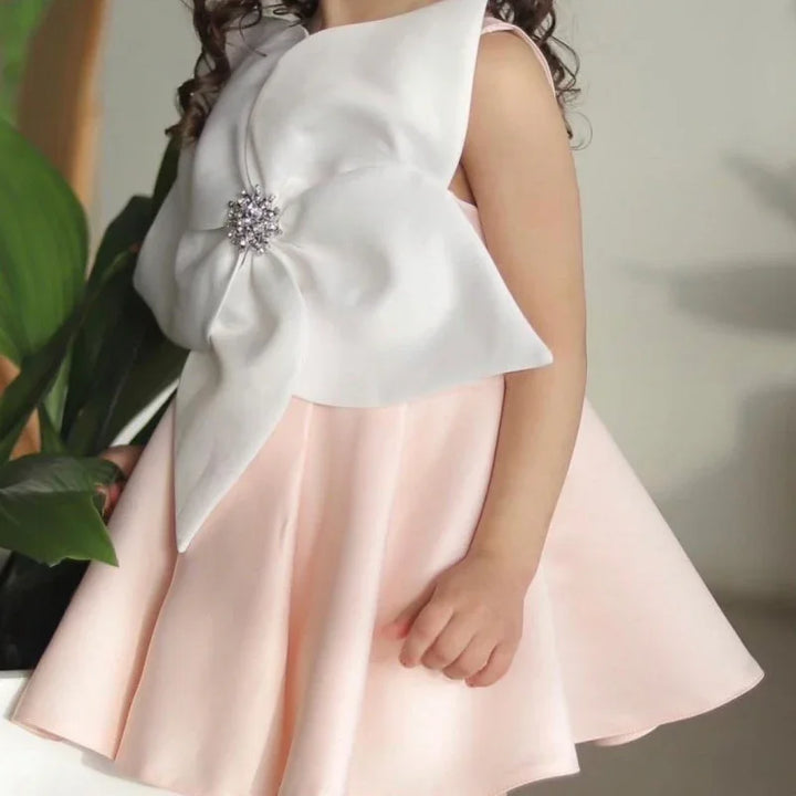 Close-up of a child wearing a pink dress with a large white flower decoration featuring a jeweled center