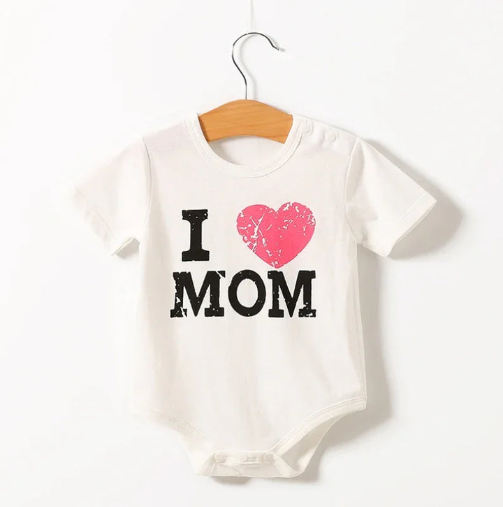 White baby onesie with distressed black text I love MOM and a pink heart, hanging on wooden hanger