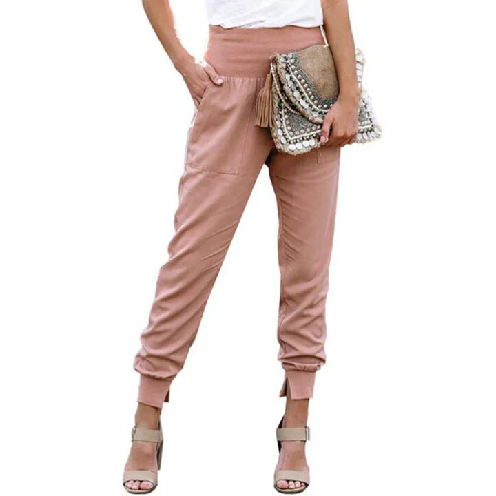 Woman wearing pink high-waisted jogger pants with cuffed ankles, holding embellished clutch bag