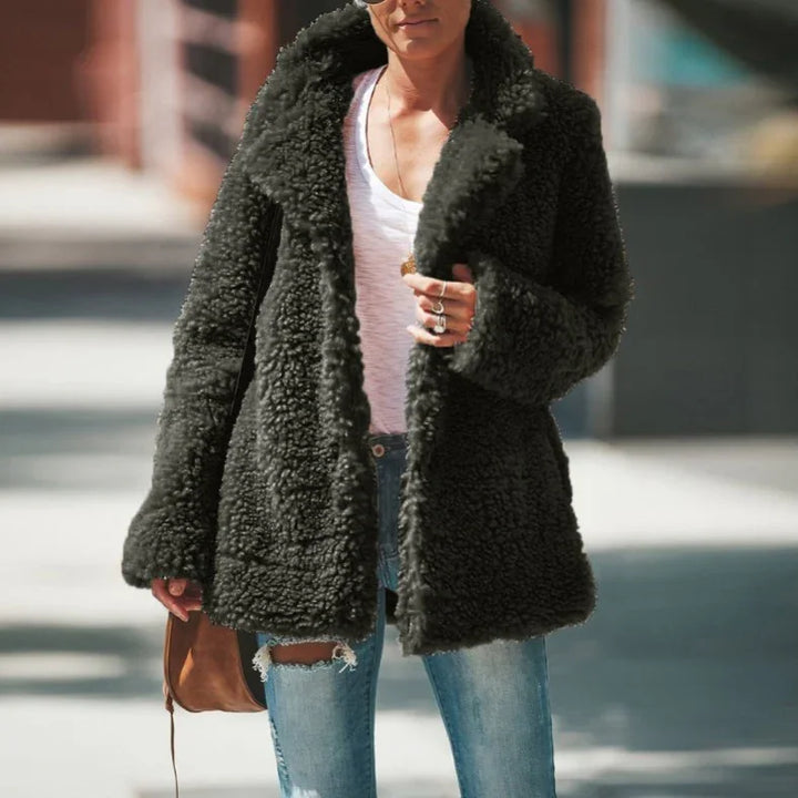 Woman wearing black faux shearling teddy coat over white t-shirt and ripped jeans in urban setting