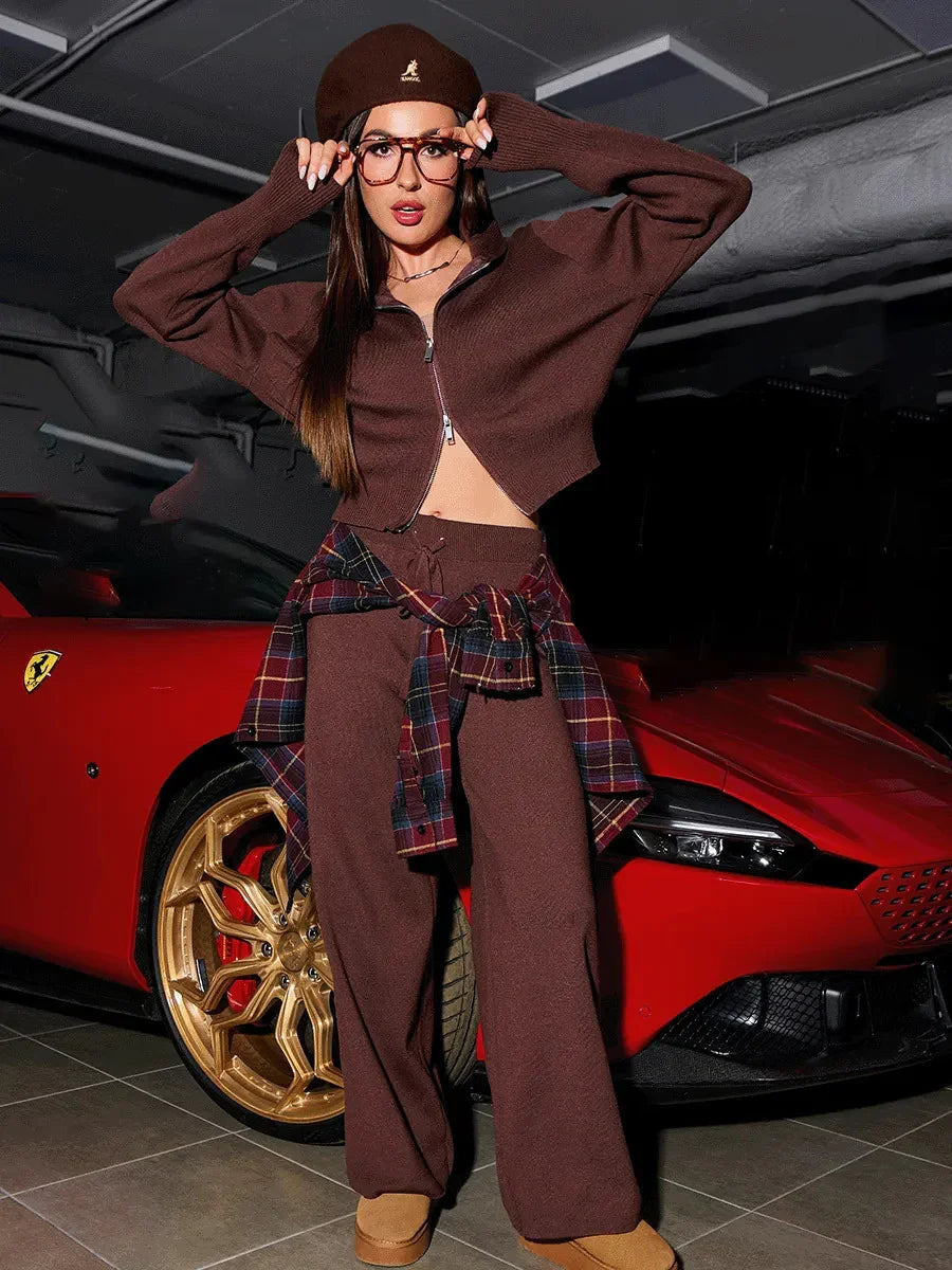 Fashionable woman in brown outfit and plaid shirt posing by red luxury sports car with gold rims