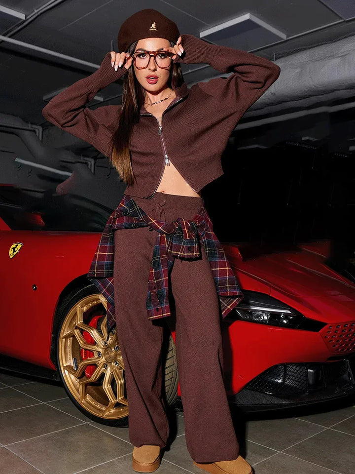 Fashionable woman in brown outfit and plaid shirt posing by red luxury sports car with gold rims