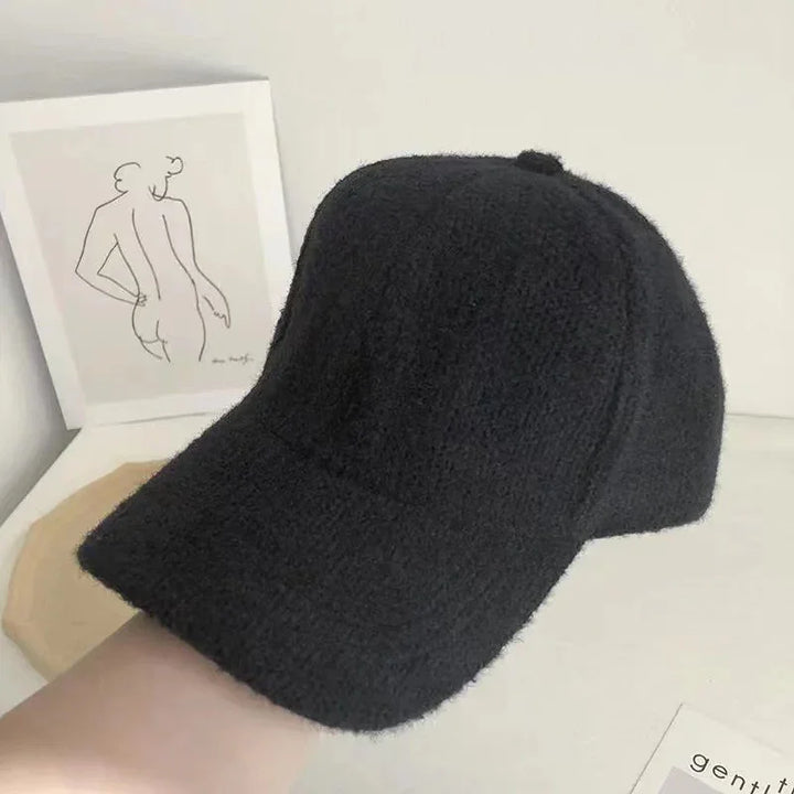 Close-up of a black textured wool baseball cap on a hand with minimalist line art in the background