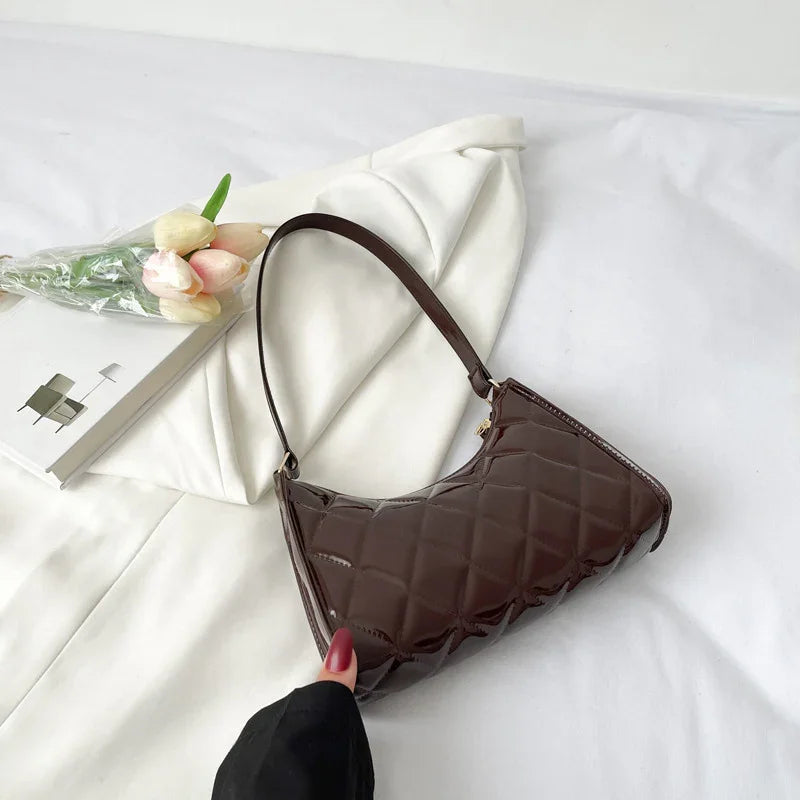 Shiny dark brown quilted leather handbag with short strap on white fabric background