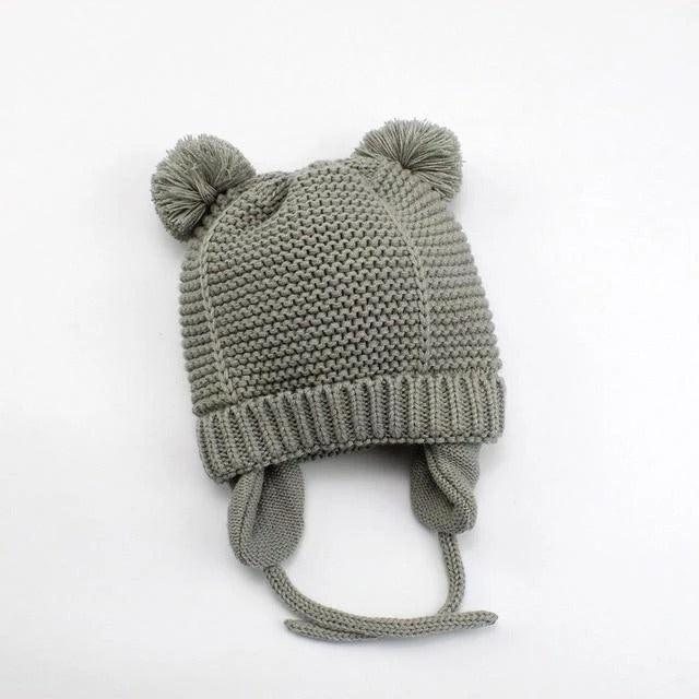 Gray knitted baby hat with earflaps and pom-poms on white background