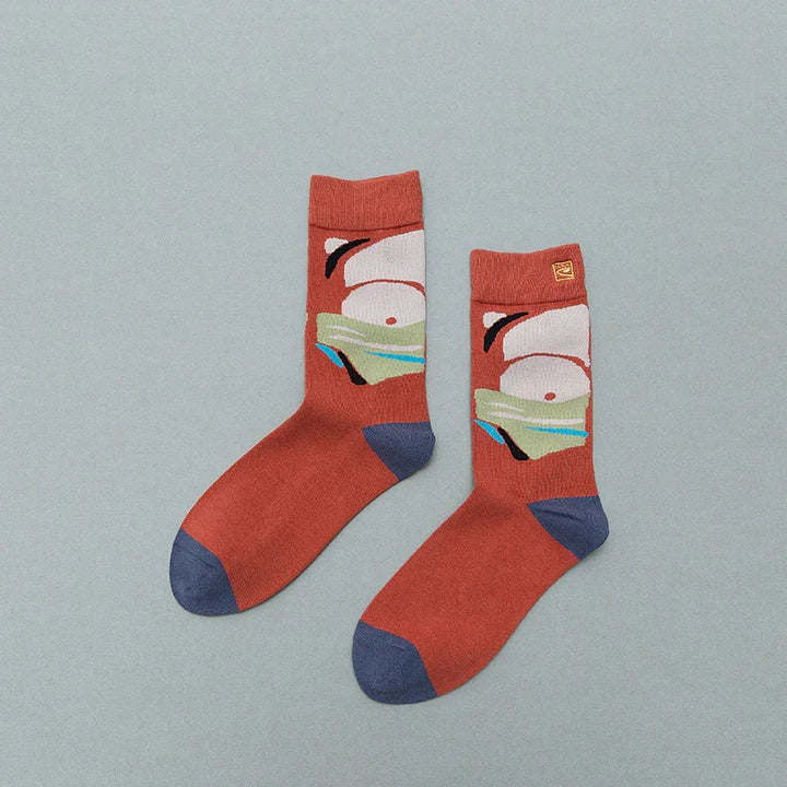 Rust-orange socks with navy toes and heels featuring abstract face art design on gray background