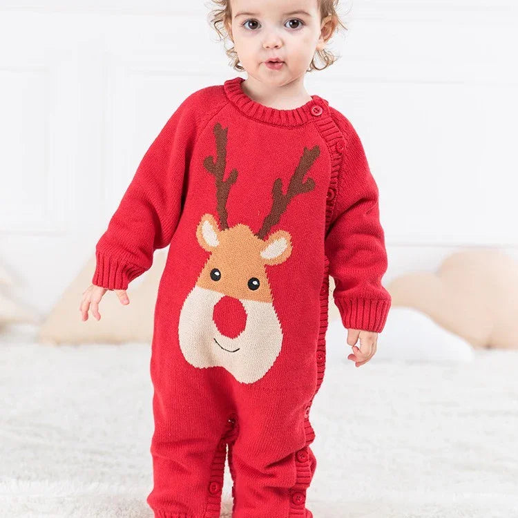 Toddler wearing a red Christmas reindeer onesie with antlers and a red nose, standing indoors