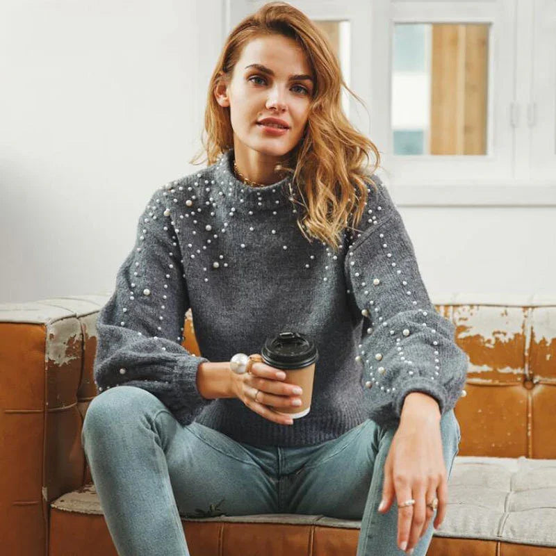 Young woman in gray pearl-studded sweater holding coffee cup sitting on vintage leather sofa