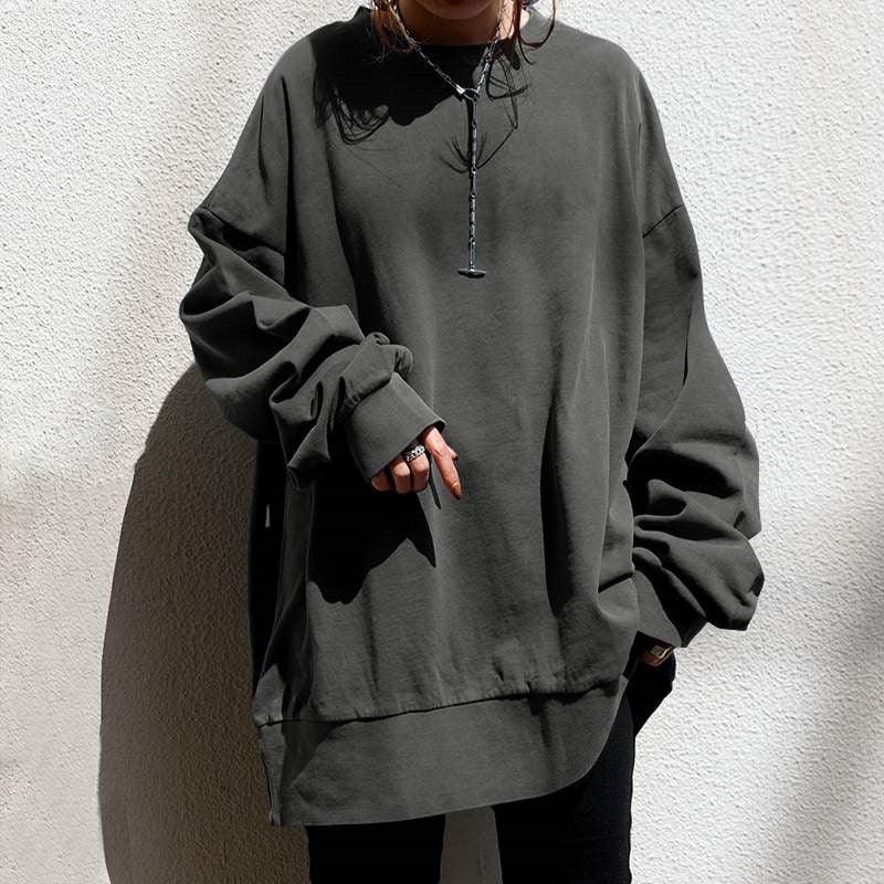 Person wearing oversized dark gray sweatshirt with long sleeves and layered hem in natural light
