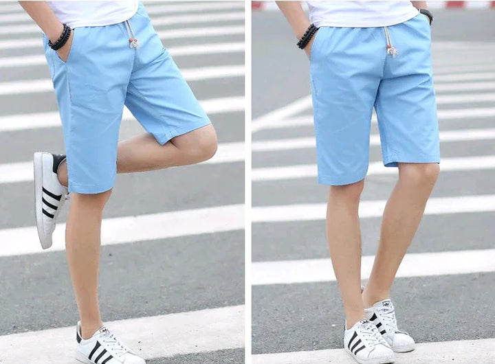 Men's light blue casual shorts with drawstring and side pockets, styled with white sneakers on street crosswalk