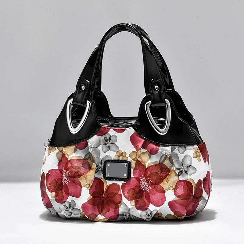 Floral pattern handbag with black patent leather handles and silver hardware on gray background