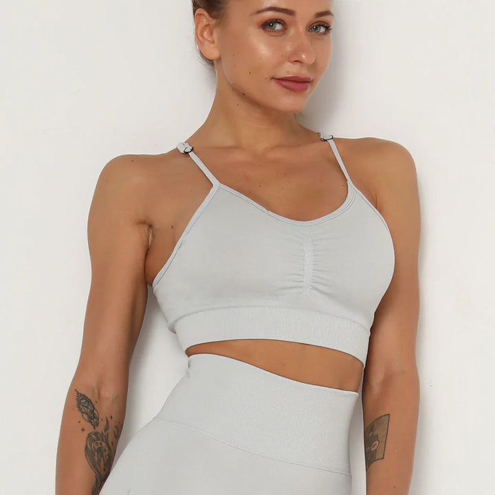 Woman wearing light gray seamless sports bra and high-waisted leggings with tattoos on arms