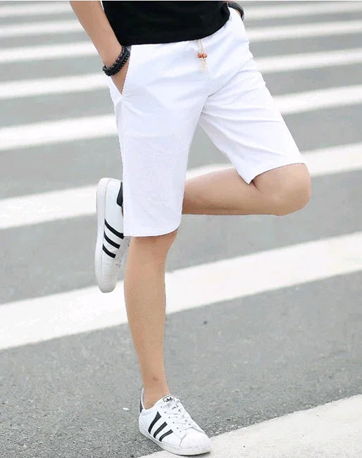 Man wearing white casual shorts and black and white sneakers standing on a crosswalk