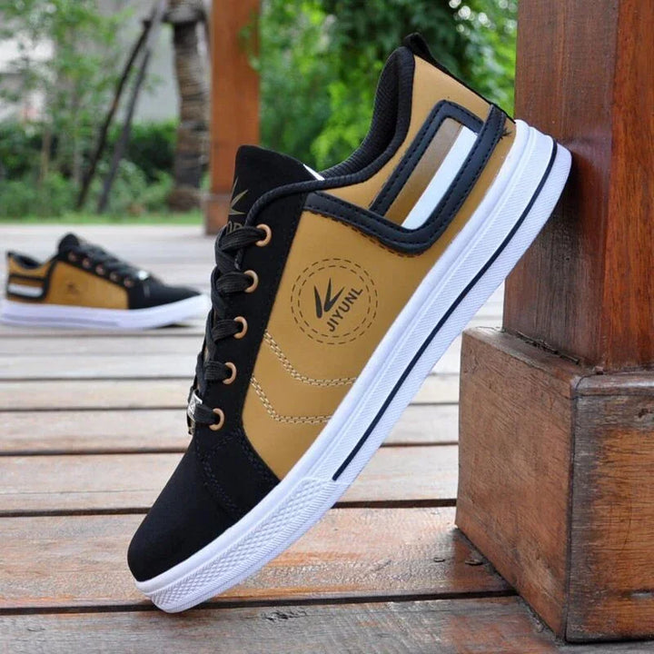 Black and tan Jiyunl casual sneakers with white soles resting on wooden deck outdoors