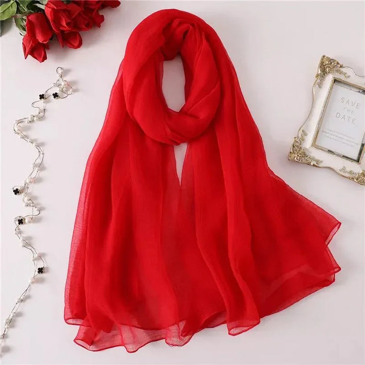 Elegant sheer red scarf displayed flat with red roses, decorative photo frame, and pearl string on white background