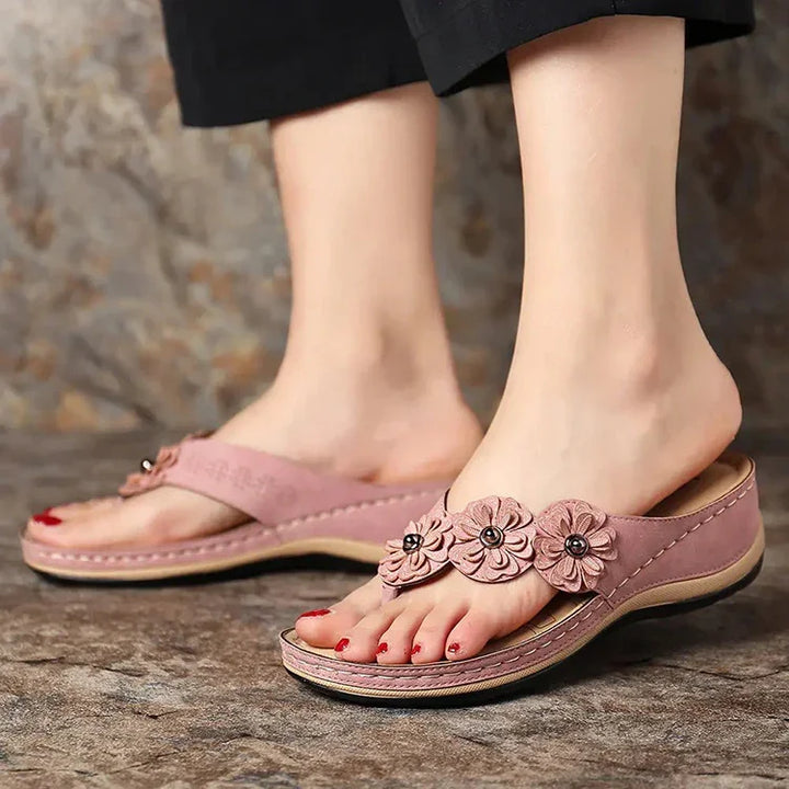 Pink floral leather sandals with decorative flowers worn on feet with red nail polish
