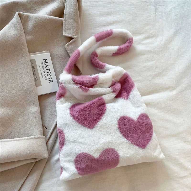 Soft plush white handbag with large pink heart patterns on a beige fabric background