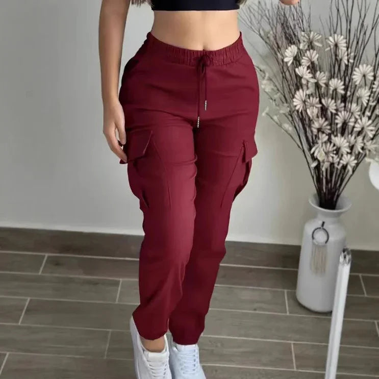Woman wearing burgundy cargo jogger pants with pockets and white sneakers on tiled floor