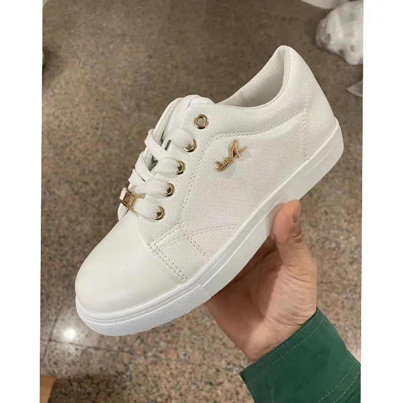 White casual sneaker with gold eyelets and logo held in hand on speckled floor