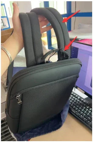 Black padded laptop bag held by hand with two cushioned straps and a front zipper pocket on office desk