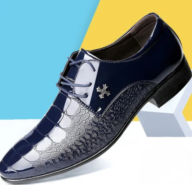 Shiny navy blue men's dress shoe with crocodile texture and silver cross emblem on geometric background