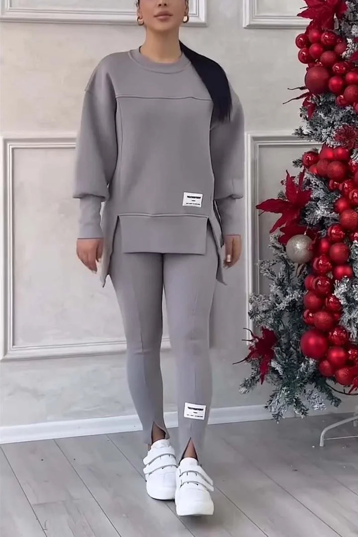 Woman wearing gray loungewear set with tunic sweater and leggings, white sneakers, beside red Christmas decorations