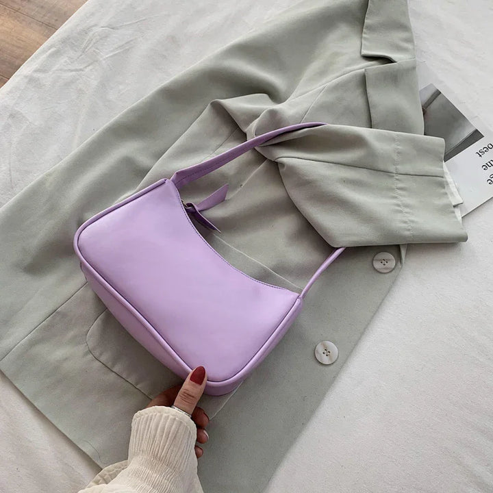 Lavender leather shoulder bag on beige blazer with hand holding the bag, fashion accessory