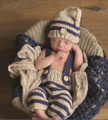 Newborn baby sleeping in knitted beige and navy striped outfit with hat, cozy blanket background