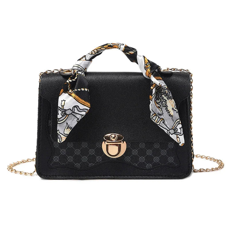 Elegant black leather handbag with gold clasp, chain strap, and decorative patterned scarf handle