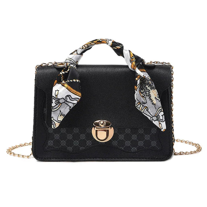 Elegant black leather handbag with gold clasp, chain strap, and decorative patterned scarf handle